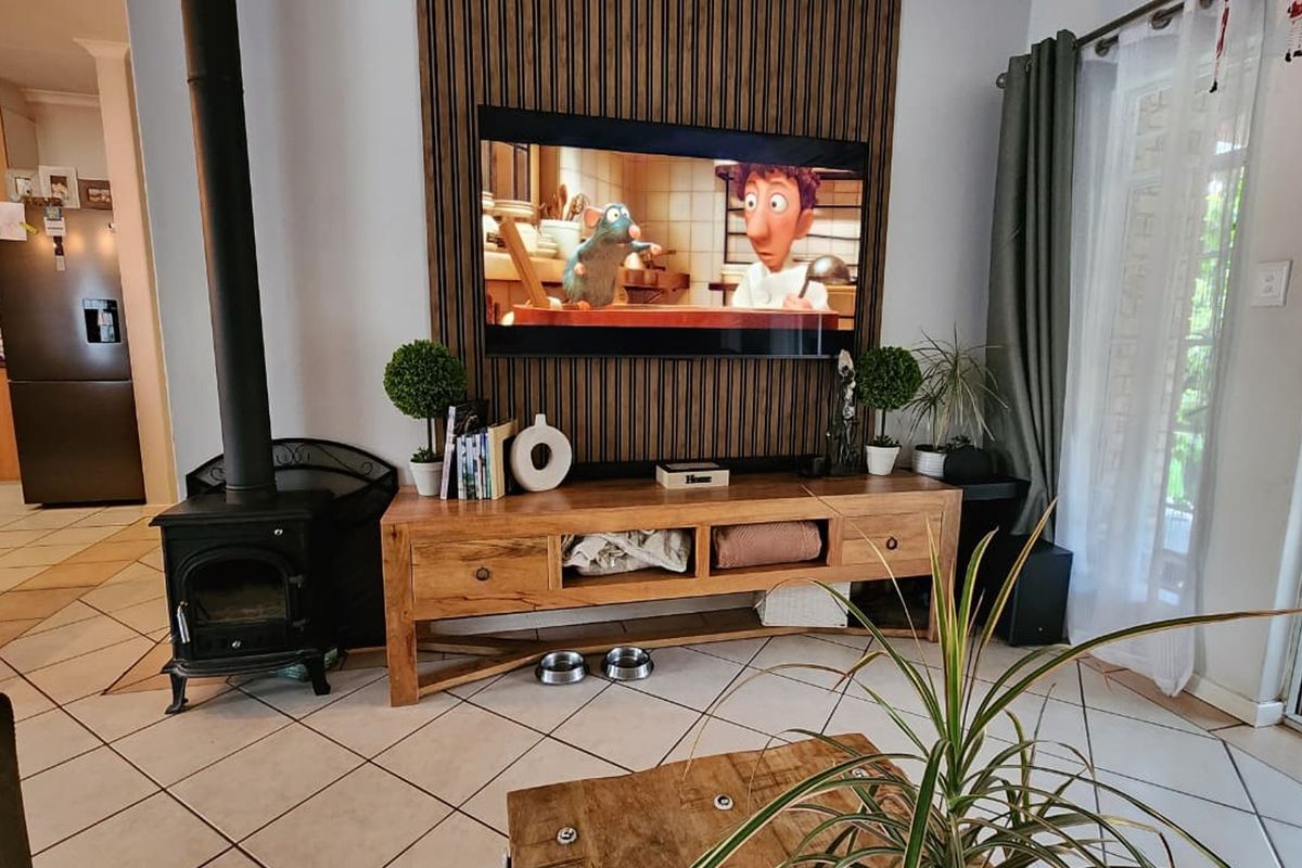 A cozy living room featuring a slatted timber accent wall, a freestanding wood-burning fireplace, and neutral ceramic floor tiles with access to the patio.