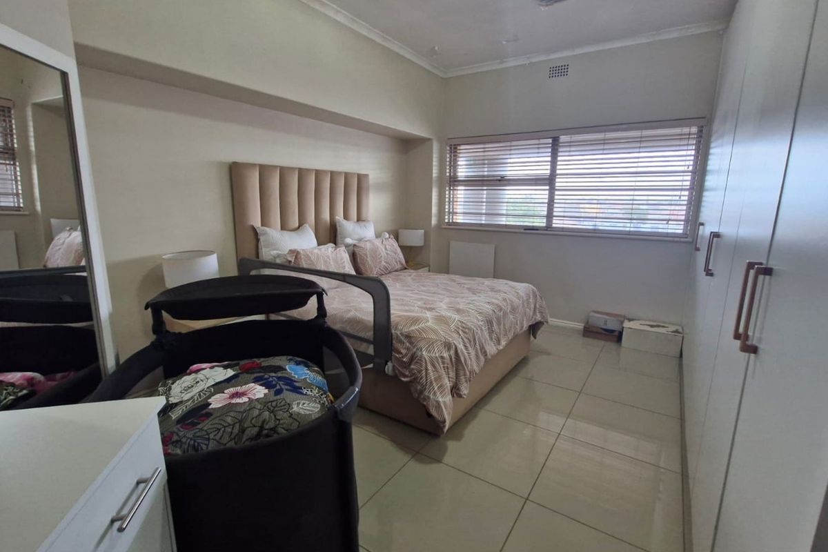 A well-maintained bedroom featuring neutral tiled flooring, ample built-in cupboard storage, and venetian blinds for privacy.