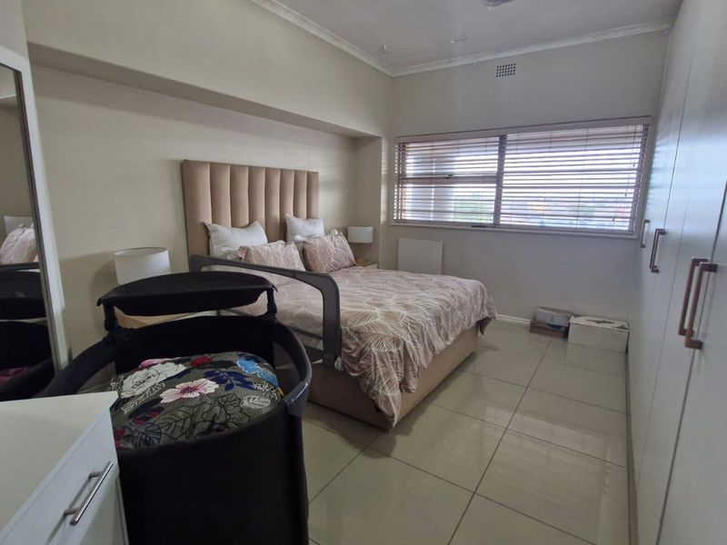 A well-maintained bedroom featuring neutral tiled flooring, ample built-in cupboard storage, and venetian blinds for privacy.