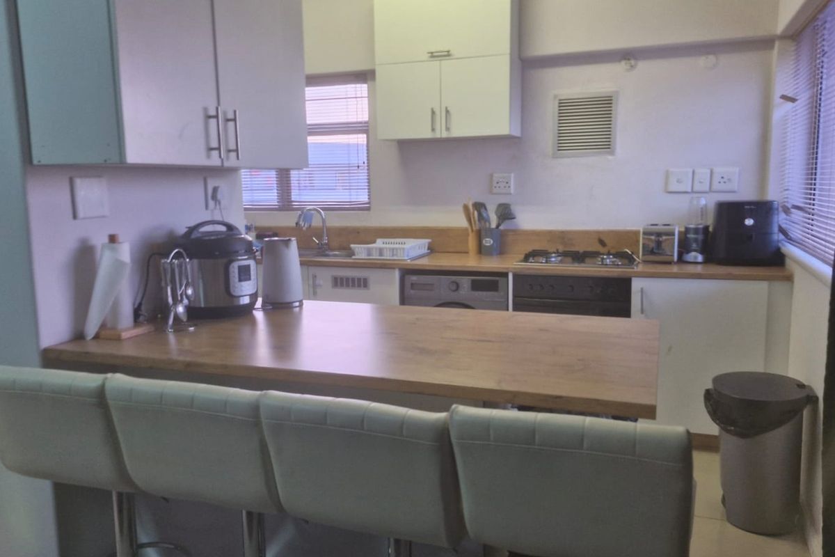 A functional kitchen featuring white cabinetry, wooden countertops, a built-in oven, gas hob, and a breakfast bar area.
