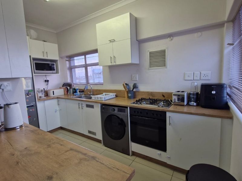 Functional kitchen featuring white cabinetry, wood-look countertops, integrated appliances including a gas hob, oven, and washing machine, with natural light from large windows.