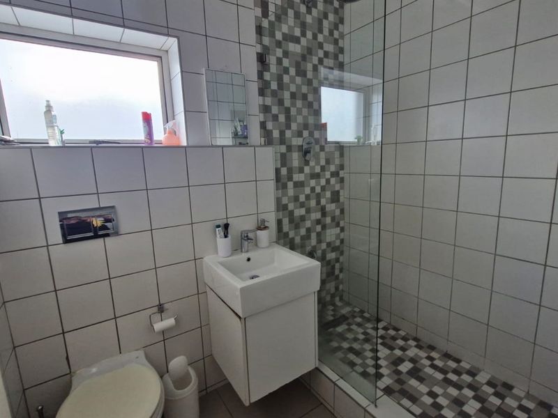 A modern bathroom featuring a wall-mounted vanity, a glass-enclosed shower with mosaic tile accents, and a wall-mounted toilet.