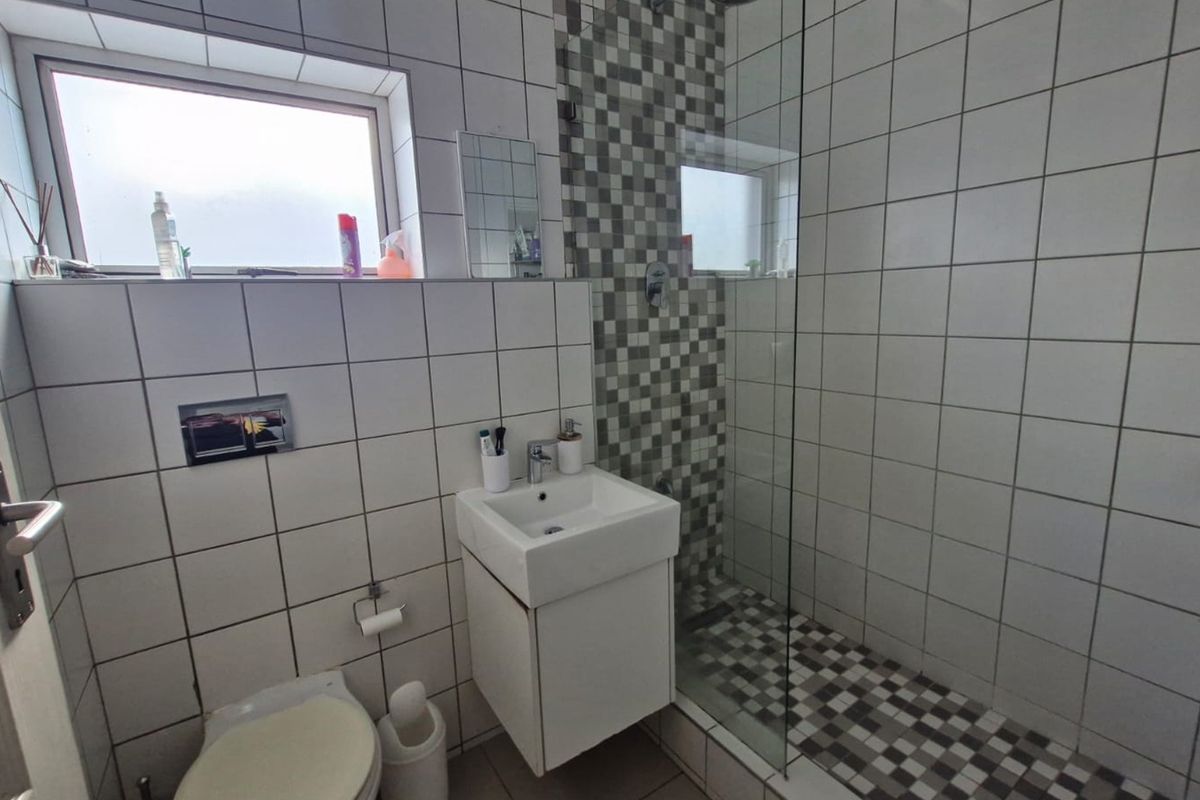 A modern bathroom featuring a wall-mounted vanity, a glass-enclosed shower with mosaic tile accents, and a wall-mounted toilet.