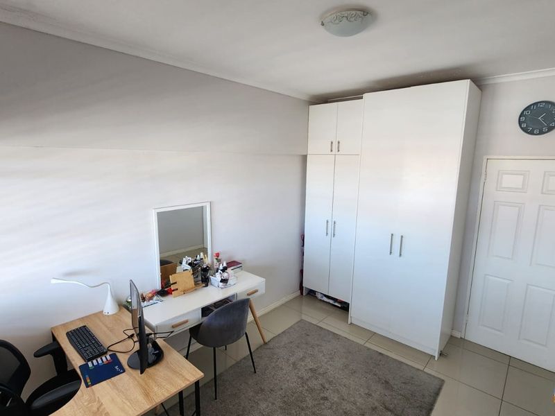 A bedroom featuring tiled flooring and a white built-in wardrobe, providing functional storage space within the room.