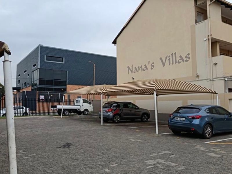 Exterior view of Nana's Villas apartment complex featuring a paved parking area with shade cloth carports and perimeter security fencing.