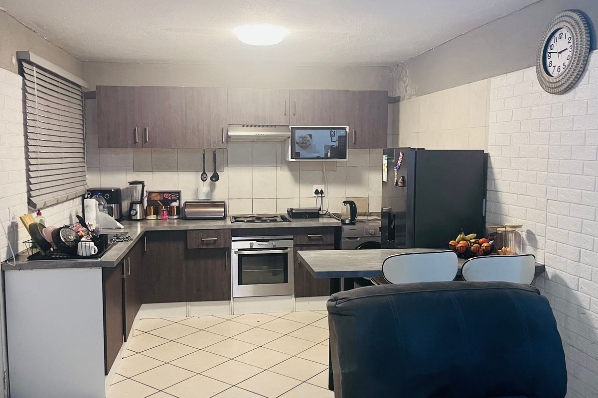 A functional kitchen featuring dark wood cabinetry, built-in oven and hob, tiled backsplash, and a breakfast bar, with some visible wear on wall surfaces.