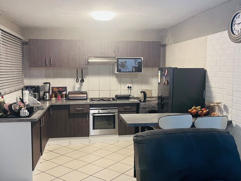 A functional kitchen featuring dark wood cabinetry, built-in oven and hob, tiled backsplash, and a breakfast bar, with some visible wear on wall surfaces.
