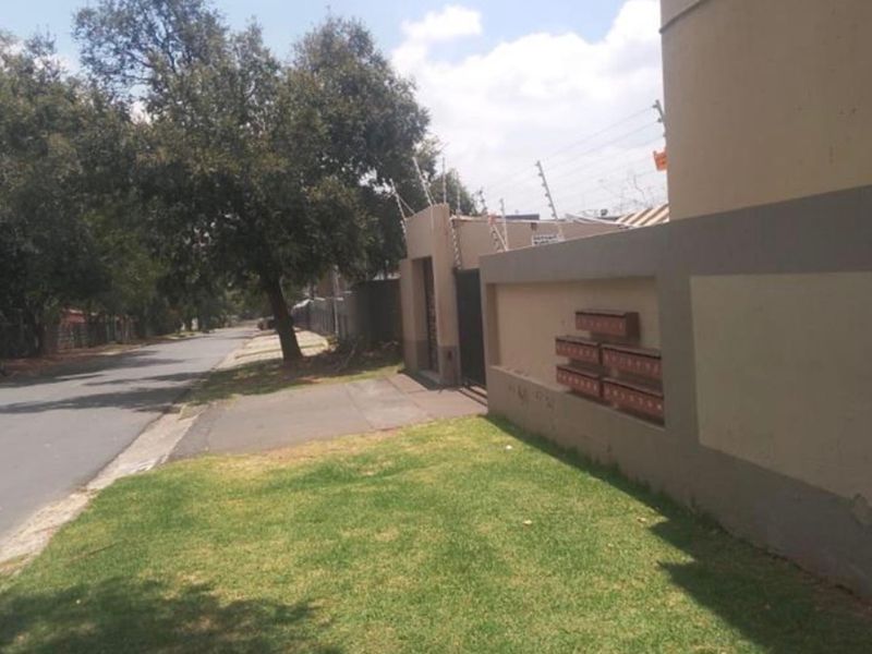 Street view of the apartment complex perimeter, featuring a boundary wall with integrated mailboxes and security electric fencing.