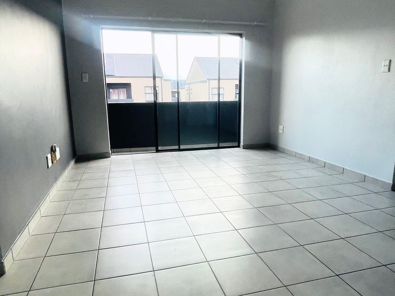 An empty, open-plan living area featuring neutral tiled flooring and a large sliding glass door providing access to an outdoor space.