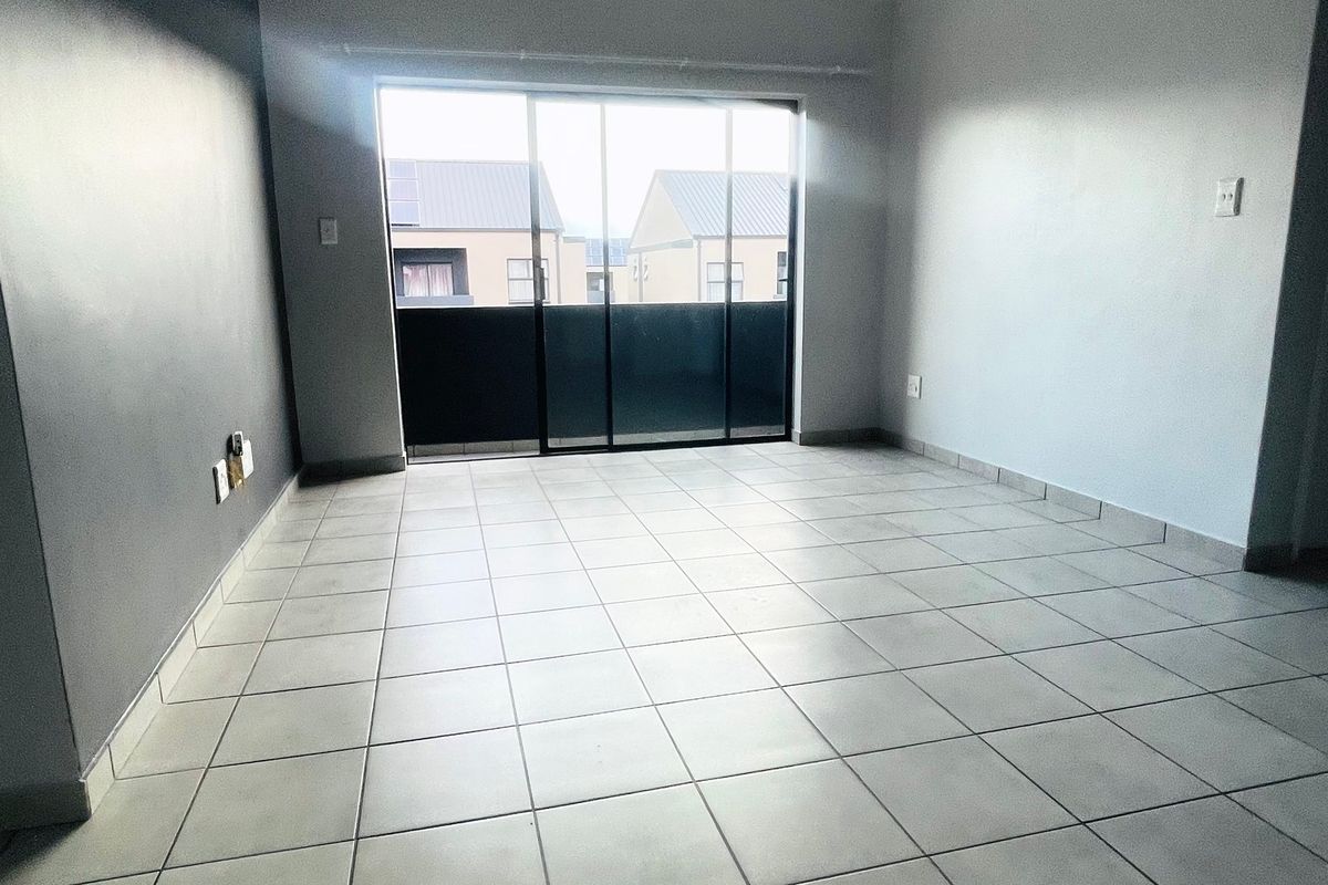 An empty, open-plan living area featuring neutral tiled flooring and a large sliding glass door providing access to an outdoor space.