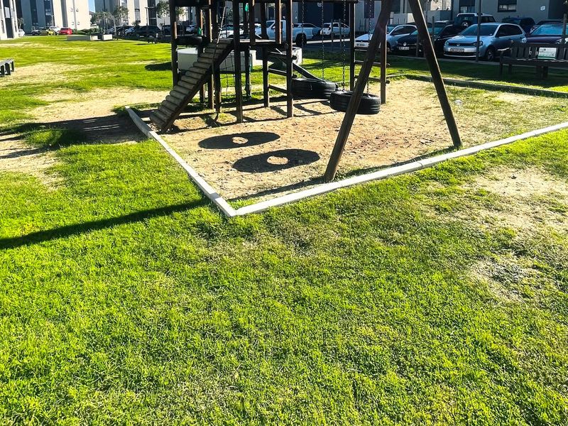 Communal garden area featuring a children's play structure with a sand pit and established lawn space within the apartment complex.