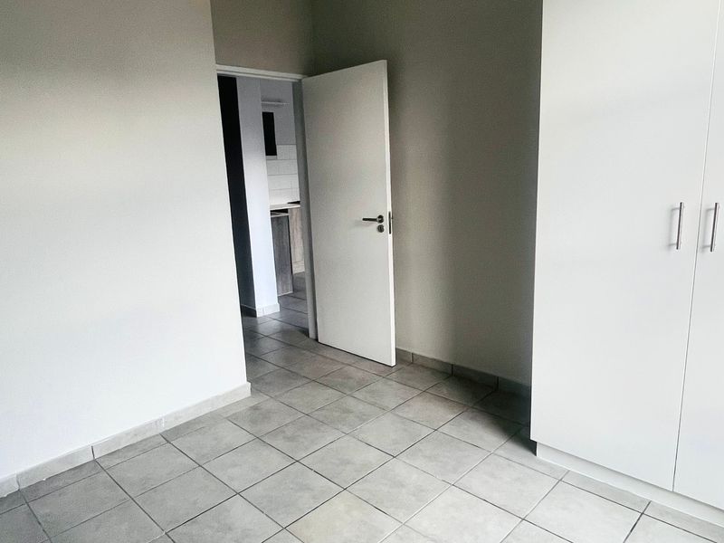 An empty bedroom featuring neutral tiled flooring and built-in cupboards, with a doorway leading to an adjacent space.