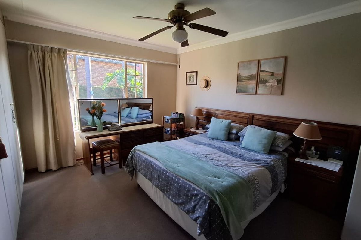 A well-proportioned bedroom featuring built-in cupboards, a ceiling fan, and carpeted flooring, offering a comfortable and functional living space.