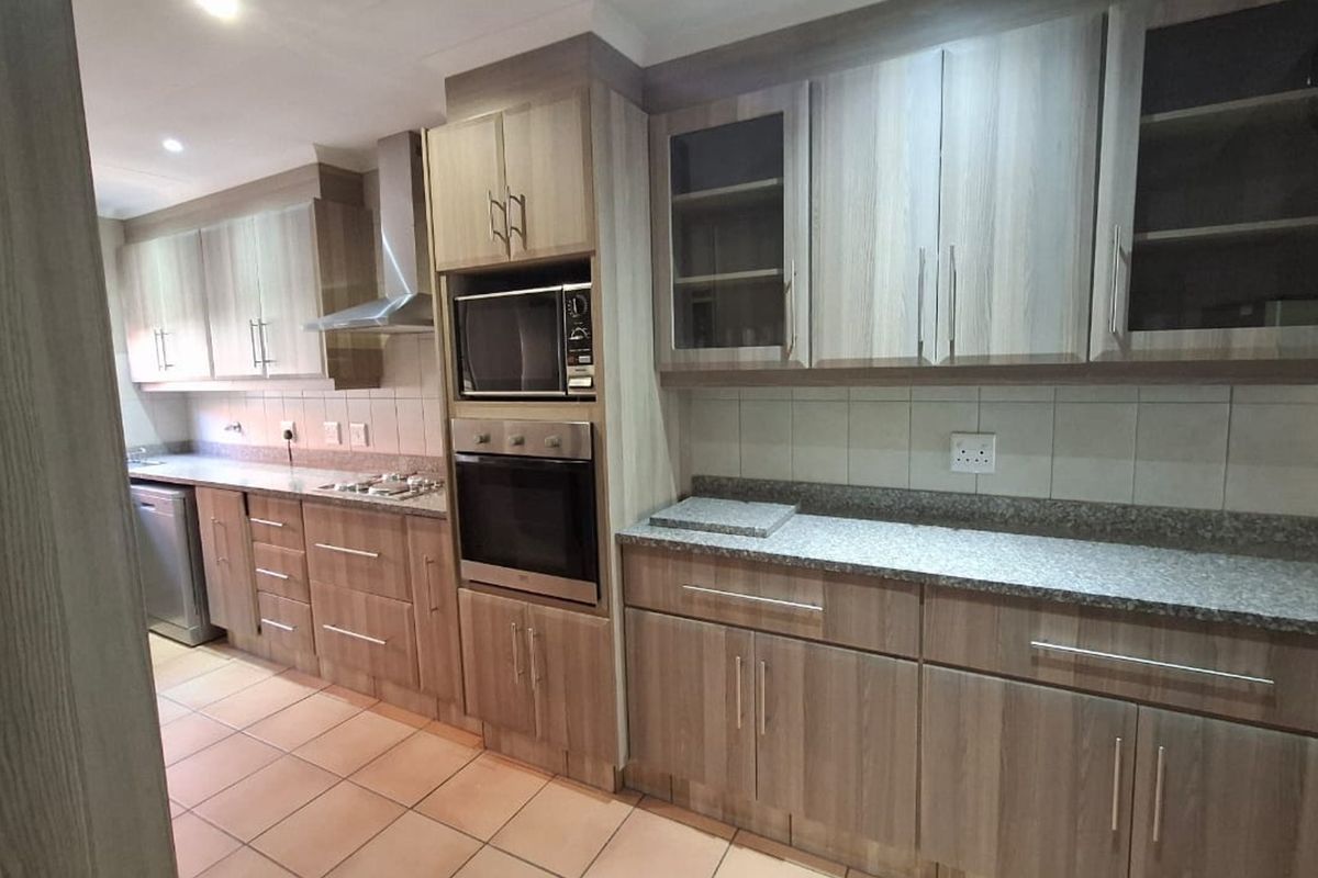 A functional kitchen featuring wood-look laminate cabinetry, granite countertops, built-in oven and microwave, stainless steel extractor fan, and tiled flooring.