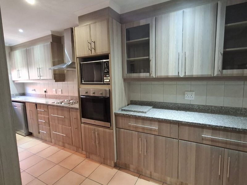A functional kitchen featuring wood-look laminate cabinetry, granite countertops, built-in oven and microwave, stainless steel extractor fan, and tiled flooring.