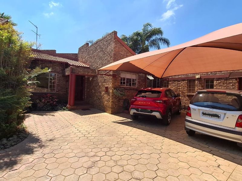 Front exterior view of the house featuring a brick facade, paved driveway, and a large shade sail covering the parking area.