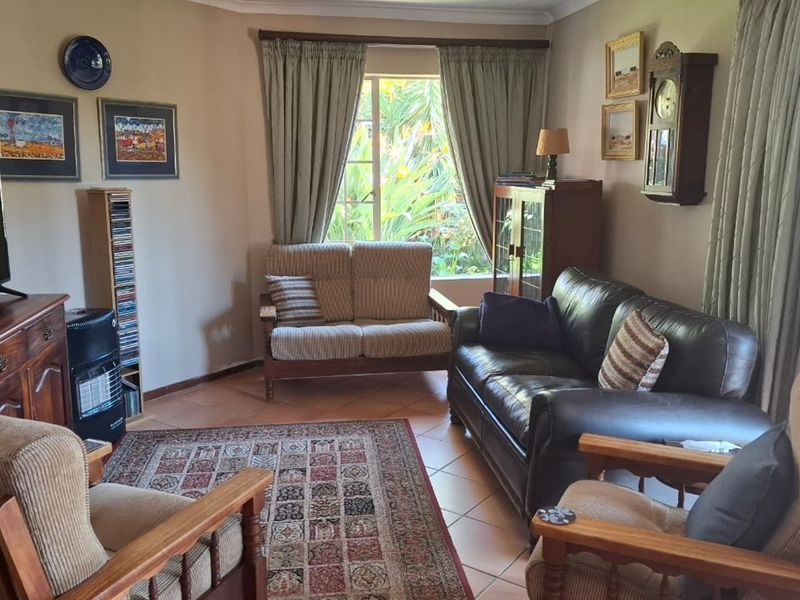 A comfortable living room featuring tiled flooring, natural light from a large window, and access to an outdoor area via a sliding glass door.