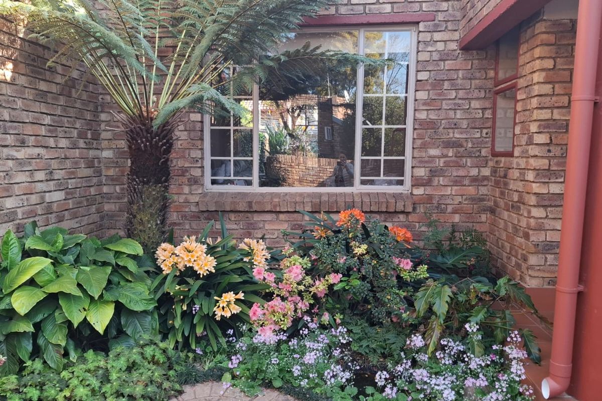 A well-maintained rear exterior view featuring face brick walls, a grid-style window, and established garden landscaping with a prominent tree fern.