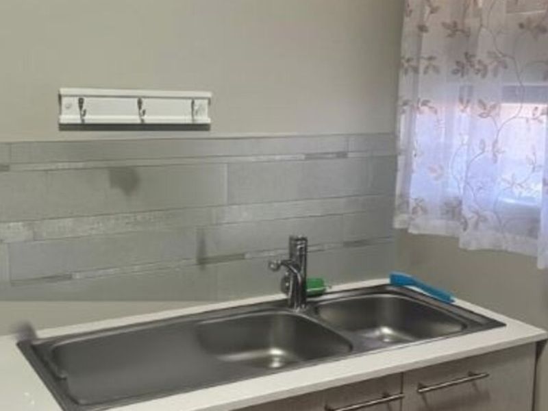 A functional laundry area featuring a stainless steel double sink, modern mixer tap, and tiled splashback with built-in cabinetry.