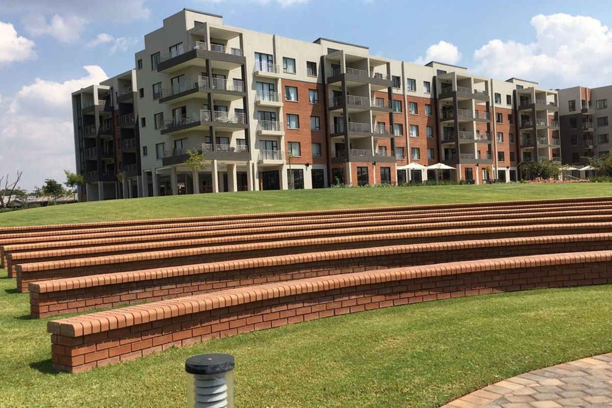 A view of the apartment complex exterior featuring tiered brick seating, landscaped lawns, and multi-story residential units with private balconies.