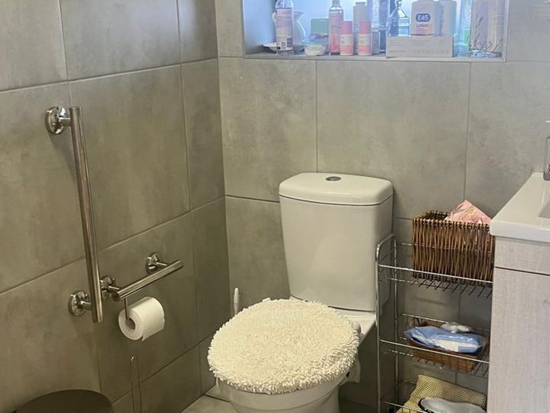 A functional bathroom featuring modern grey wall tiles, a built-in vanity with basin, a toilet, and a safety grab rail.