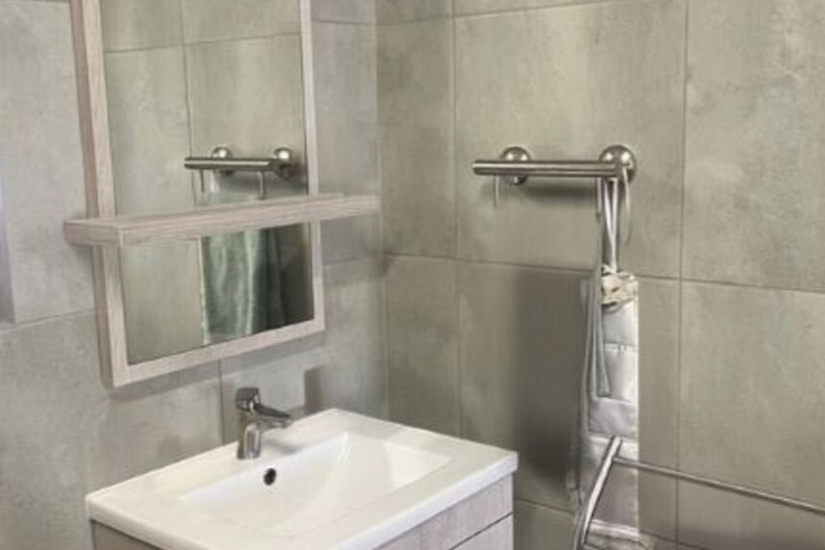 A modern bathroom featuring a vanity cabinet with a basin, mixer tap, wall mirror, and neutral grey wall tiles.