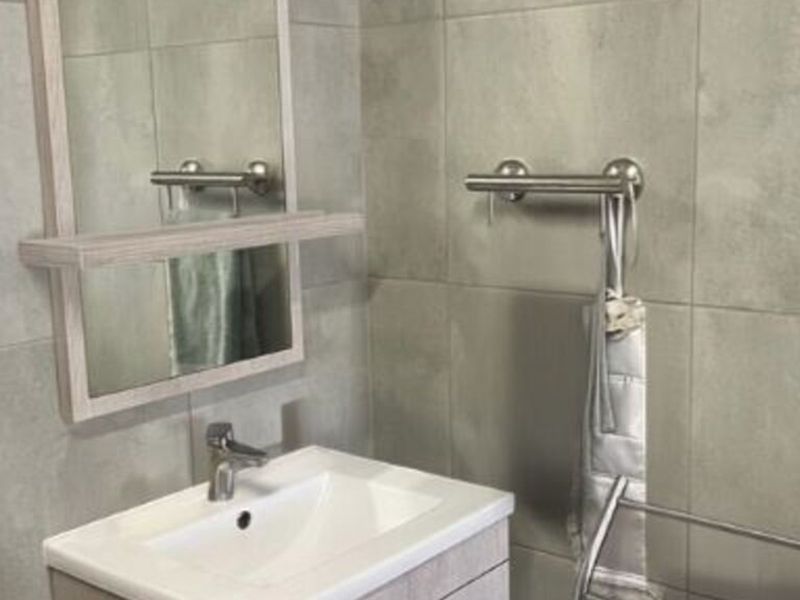 A modern bathroom featuring a vanity cabinet with a basin, mixer tap, wall mirror, and neutral grey wall tiles.