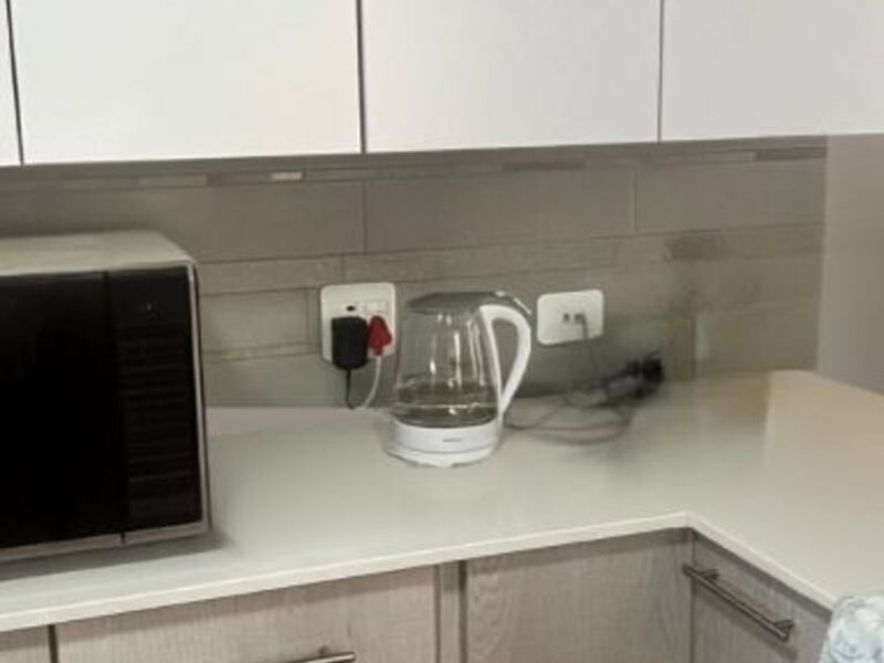 A close-up view of a kitchen workspace featuring modern white cabinetry, stone countertops, and a tiled backsplash with integrated electrical outlets.