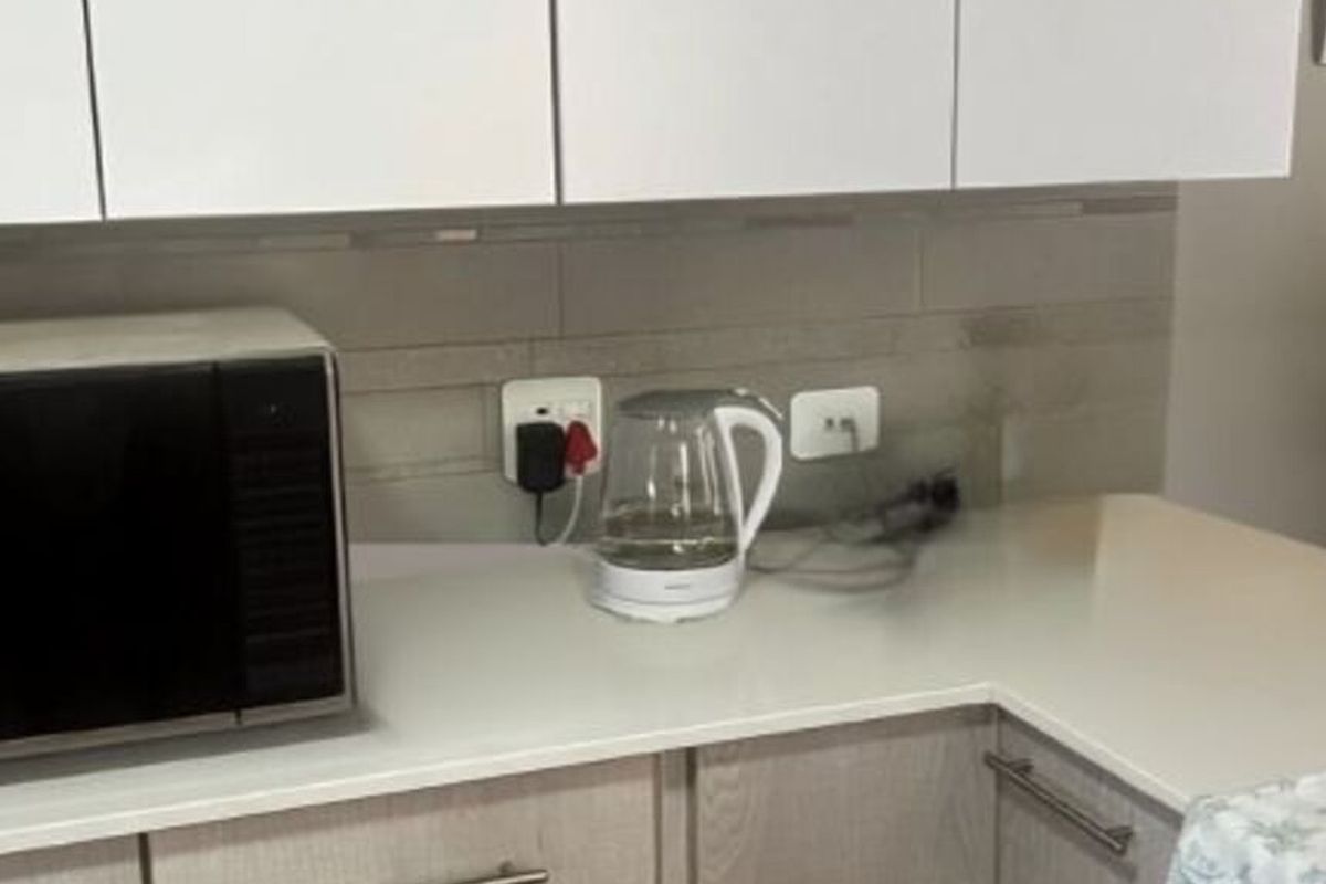 A close-up view of a kitchen workspace featuring modern white cabinetry, stone countertops, and a tiled backsplash with integrated electrical outlets.