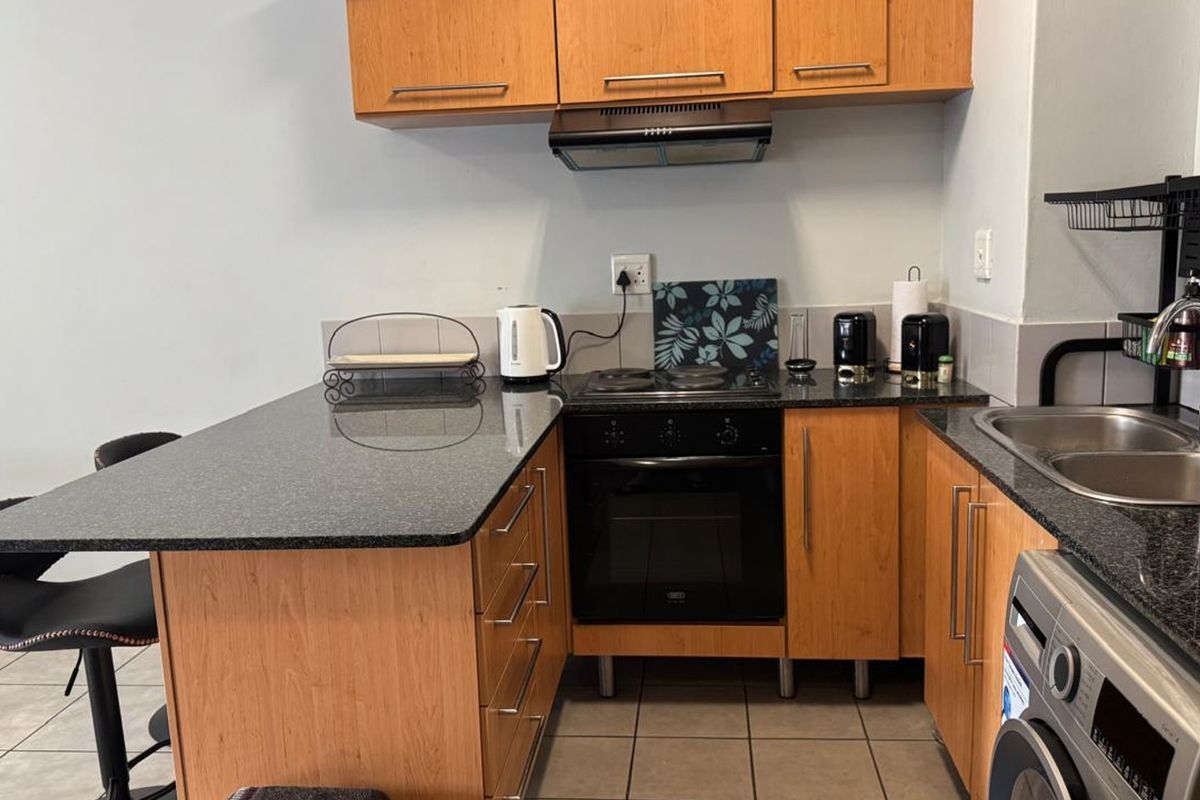 A functional kitchen featuring wood-finish cabinetry, granite countertops, a built-in oven with hob, and tiled flooring.