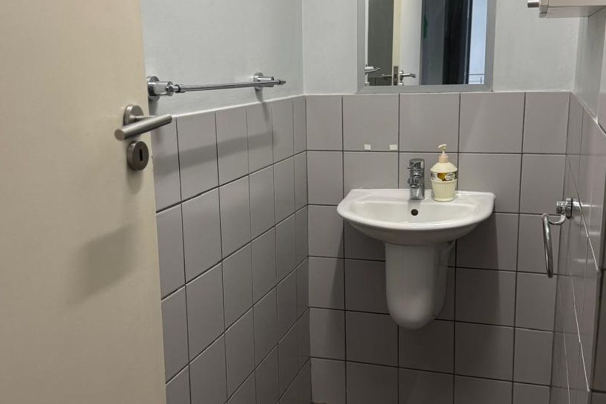 A compact bathroom featuring a pedestal basin with a chrome mixer tap, tiled walls, and a wall-mounted mirror.