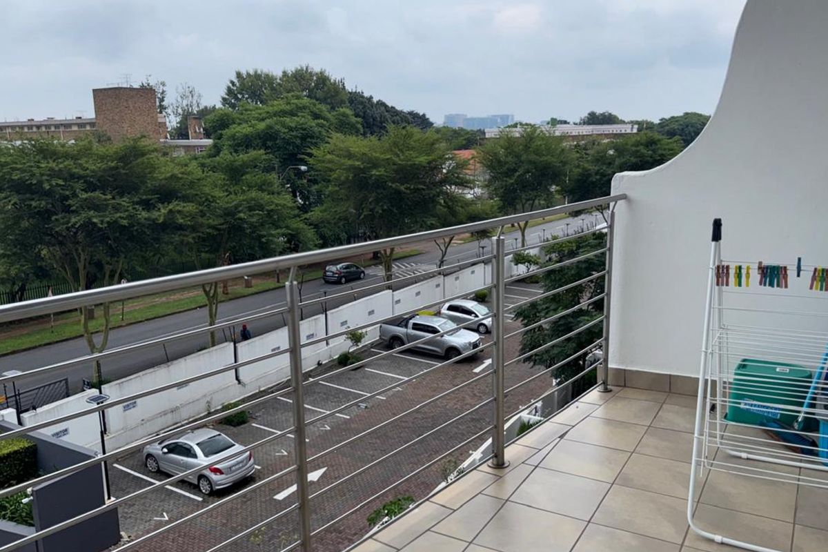 A balcony featuring tiled flooring and a stainless steel balustrade, offering an elevated view of the street and parking area.