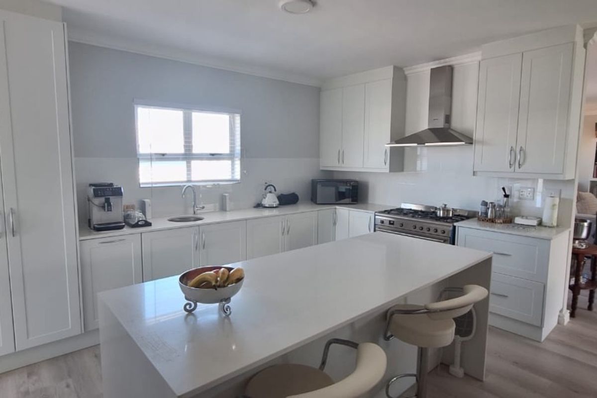 Modern kitchen featuring white cabinetry, stone countertops, a central island with breakfast bar seating, and stainless steel appliances.