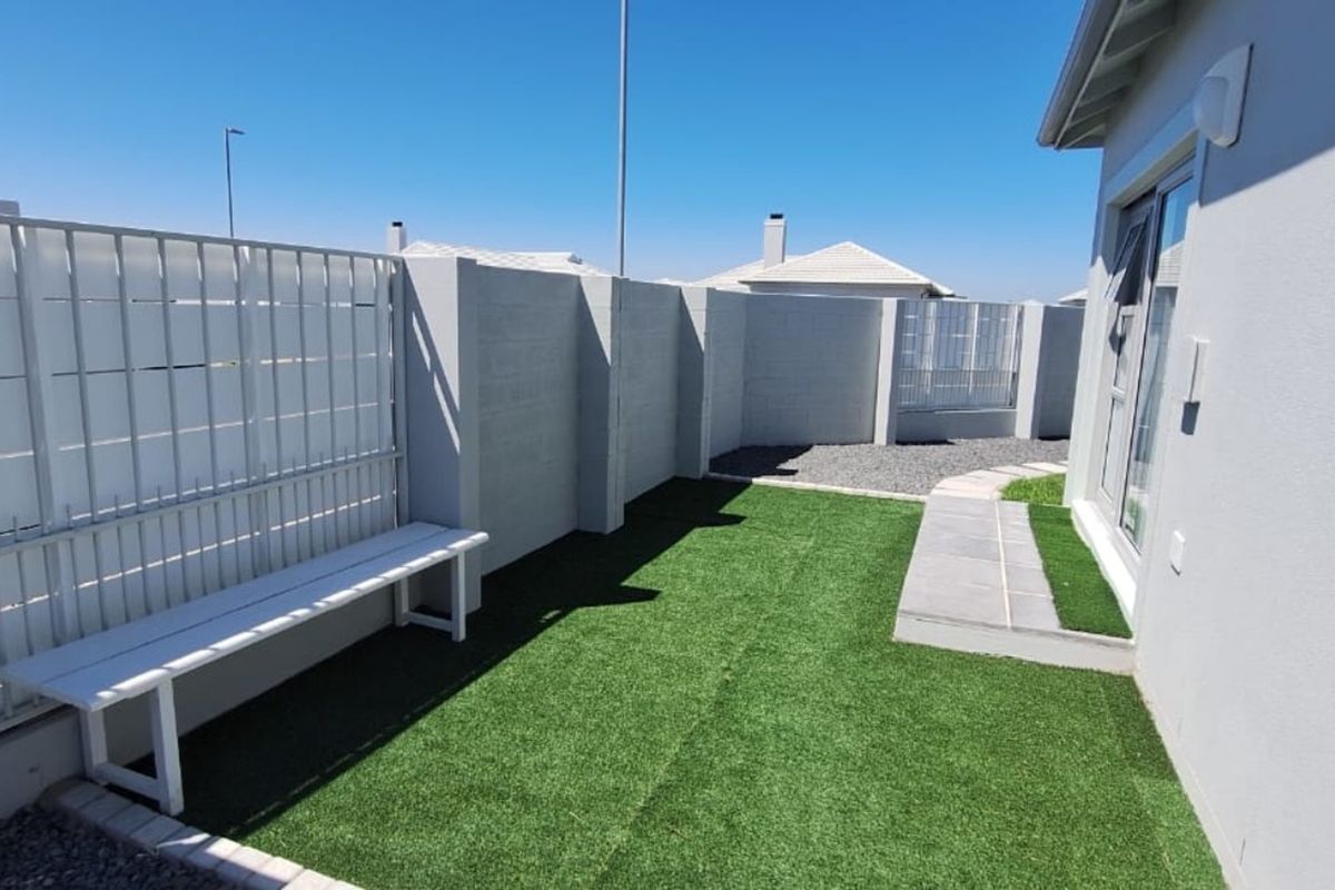 A well-maintained rear garden area featuring artificial turf, a paved walkway, and a secure boundary wall, providing a clean and low-maintenance outdoor space.