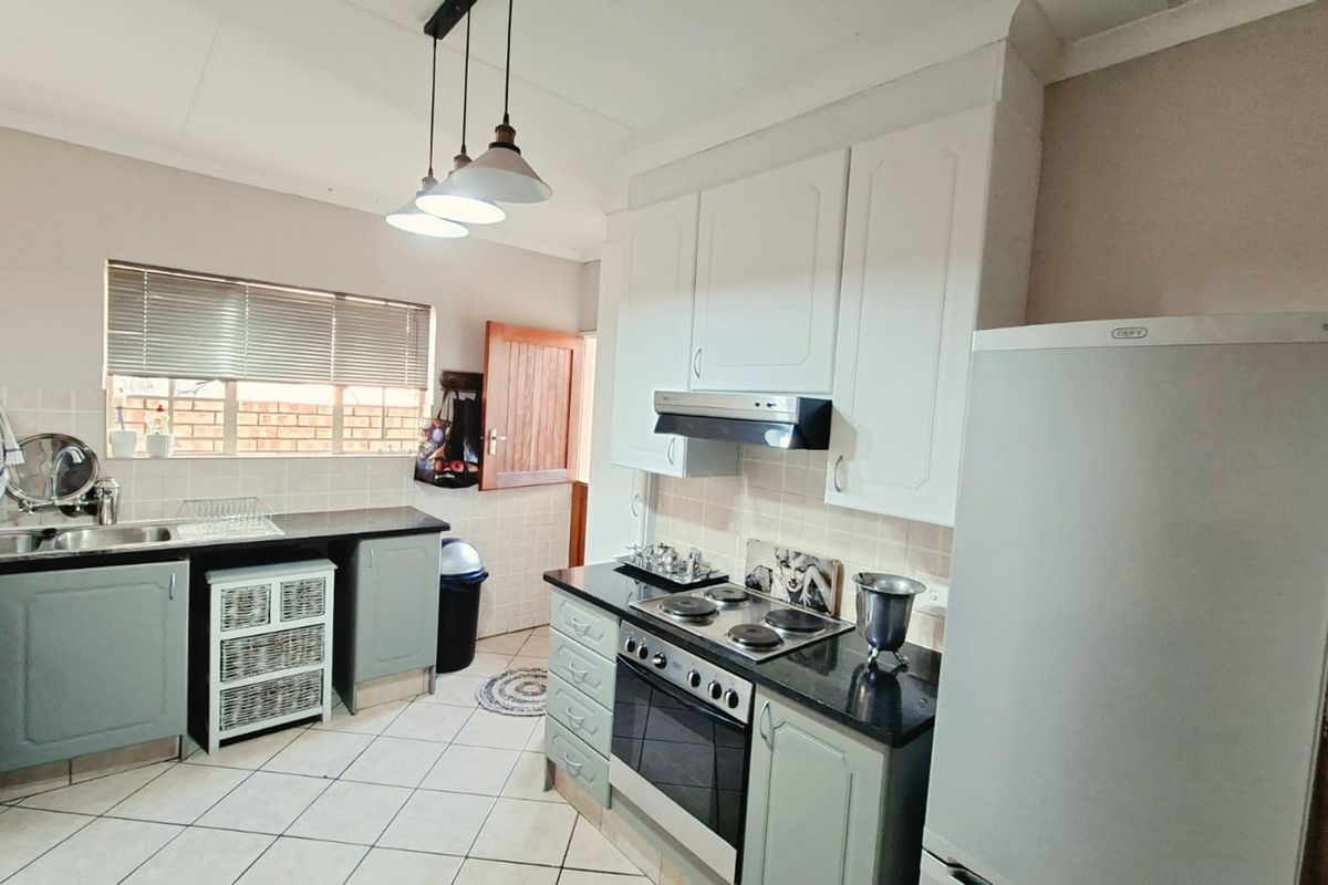 A functional kitchen featuring built-in cabinetry, a tiled backsplash, an electric hob with an extractor fan, and a double sink with tiled flooring.
