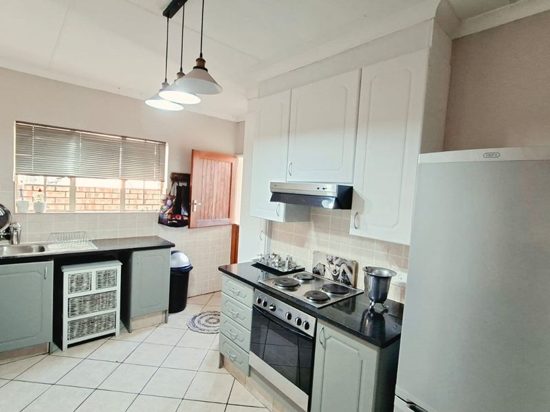 A functional kitchen featuring built-in cabinetry, a tiled backsplash, an electric hob with an extractor fan, and a double sink with tiled flooring.