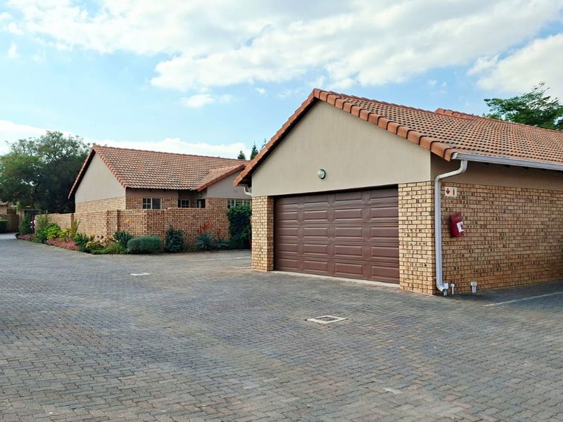 Exterior view of a townhouse complex featuring facebrick facades, tiled roofing, and paved driveway access to a private garage.