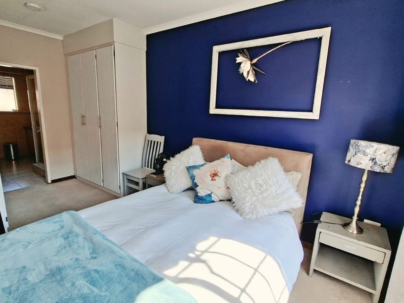 A bedroom featuring a bold blue accent wall, built-in cupboards, and direct access to an adjoining bathroom.