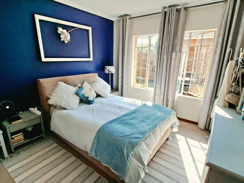 A well-lit bedroom featuring a bold blue accent wall, carpeted flooring, and large casement windows that provide natural light.