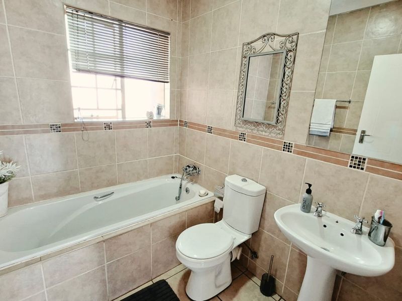 A well-maintained bathroom featuring a built-in bathtub, pedestal basin, toilet, and neutral wall tiling with decorative accents.