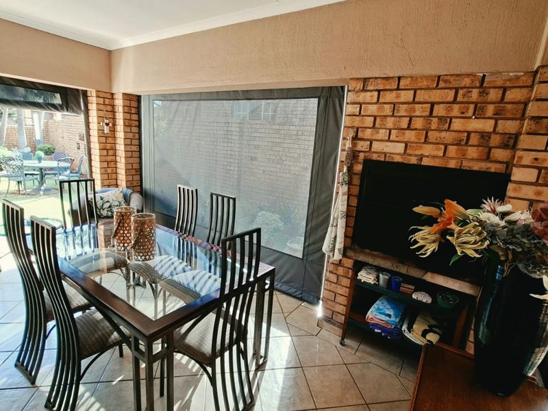 Covered patio area featuring exposed brick walls, tiled flooring, and a built-in fireplace, providing a versatile space for outdoor dining and relaxation.
