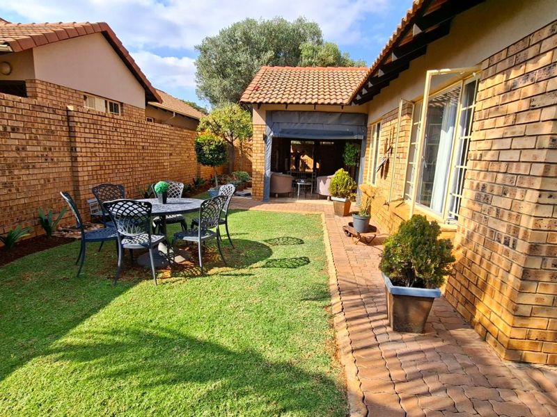 A private rear garden featuring a well-maintained lawn, paved walkway, and a covered patio area, enclosed by face brick boundary walls.