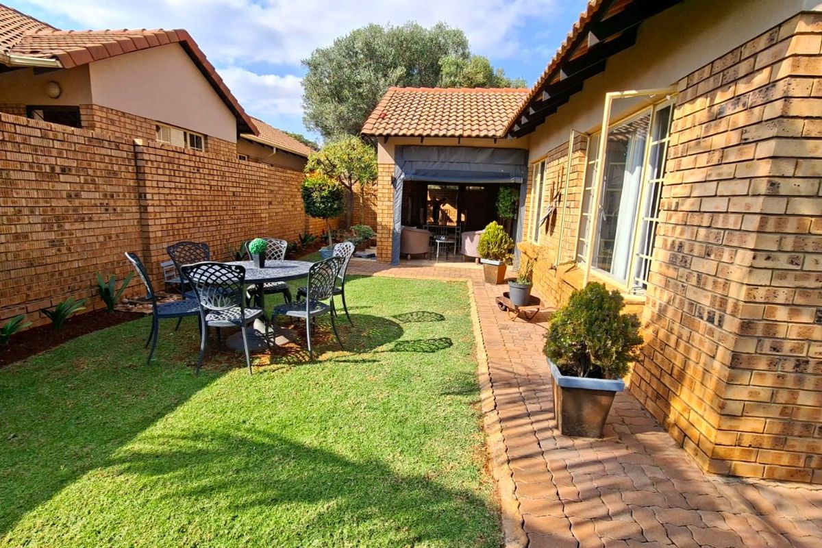 A private rear garden featuring a well-maintained lawn, paved walkway, and a covered patio area, enclosed by face brick boundary walls.