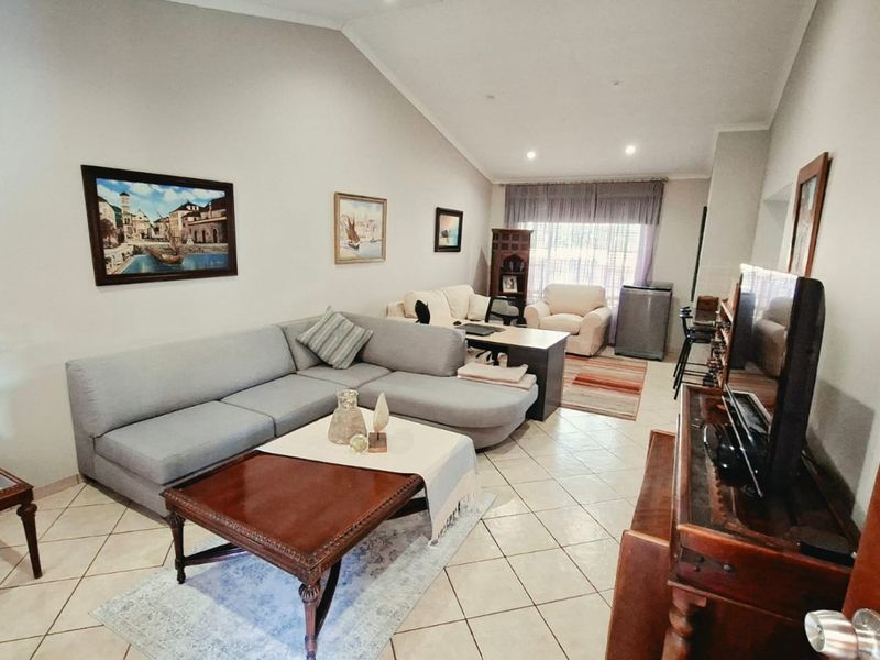 Spacious living room featuring tiled flooring, a vaulted ceiling with recessed lighting, and a neutral color palette.