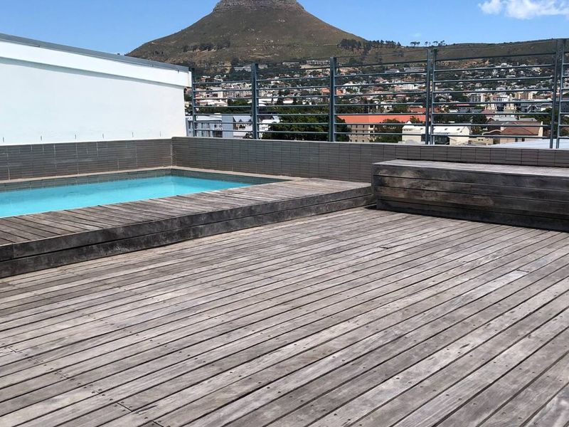 Rooftop pool area featuring timber decking, a built-in bench, and metal fencing, offering expansive mountain and city views.