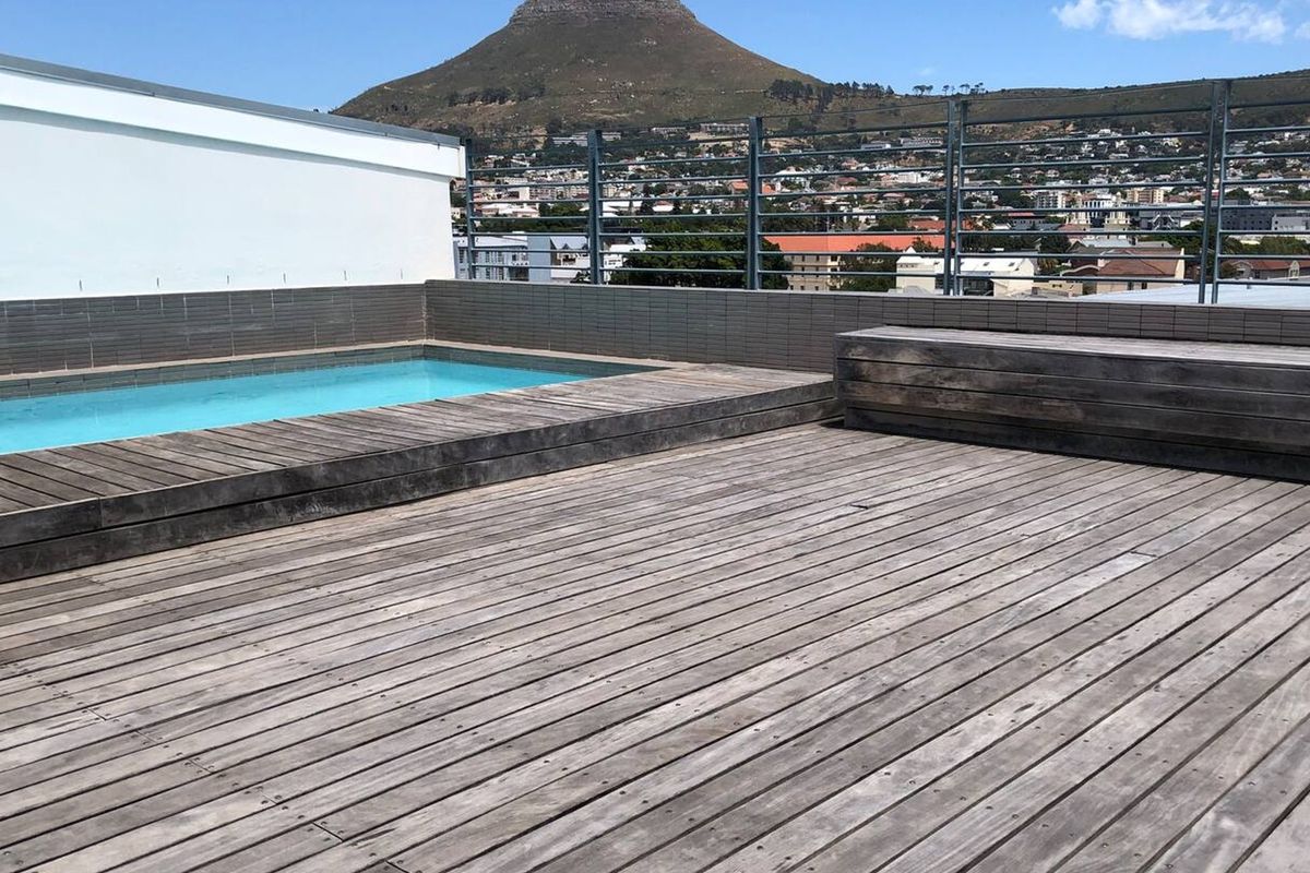 Rooftop pool area featuring timber decking, a built-in bench, and metal fencing, offering expansive mountain and city views.