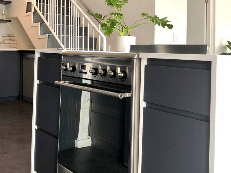 Modern kitchen featuring dark cabinetry, a stainless steel freestanding oven, and an adjacent staircase with white railings.