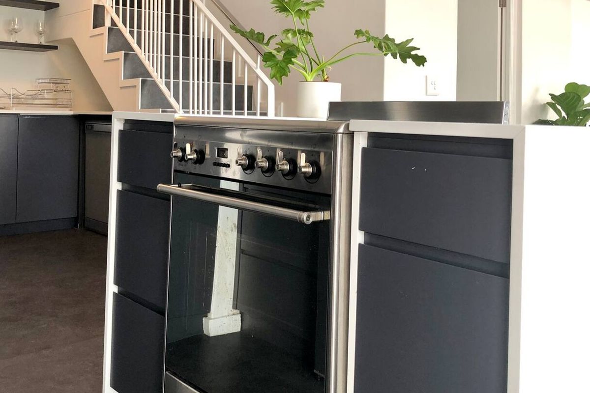 Modern kitchen featuring dark cabinetry, a stainless steel freestanding oven, and an adjacent staircase with white railings.