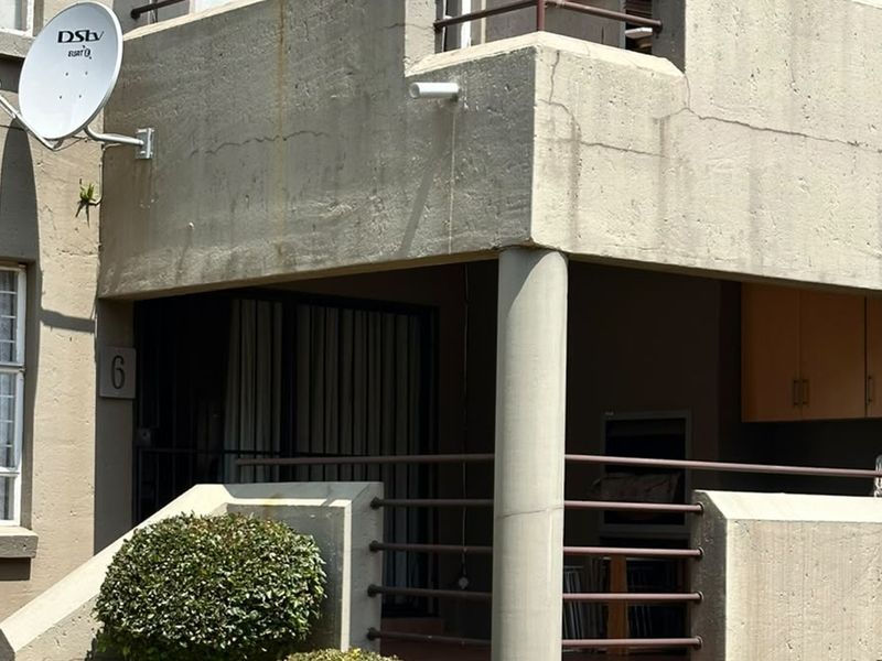 A ground-level apartment patio featuring a built-in braai, concrete structure, and metal security railings, showing signs of exterior weathering.
