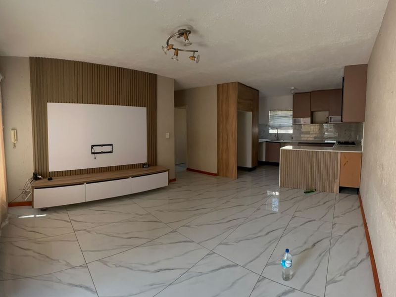 Open-plan living and kitchen area featuring marble-look floor tiles, a modern slatted wood media wall, and functional kitchen cabinetry with built-in appliances.